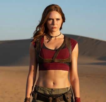 Ruby Roundhouse cosplay and group costume reference from Jumanji showing the full army green shorts, burgundy crop top, leather harness, wavy red wig, fingerless gloves, and tall riding boots assembled as the complete character look