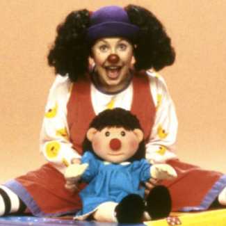 Loonette cosplay costume with rust-red wide-leg overalls, black and white striped tights, blue bowler hat, red clown nose, and black curly pigtail wig
