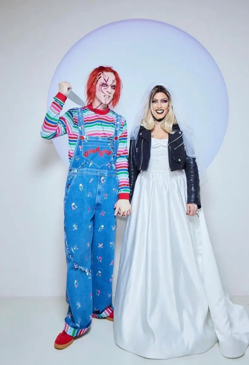 Kourtney Kardashian and Travis Barker dressed as Tiffany Valentine and Chucky for Halloween, Kourtney in the tattered bride dress and leather jacket with platinum wig and Tiffany makeup, Travis in the Chucky striped top and overalls with the scarred doll face