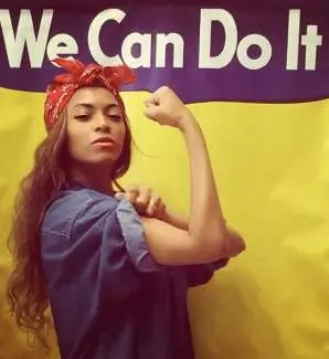 Beyonce posing as Rosie the Riveter in a denim shirt and red paisley bandana, flexing her bicep in front of a yellow We Can Do It backdrop