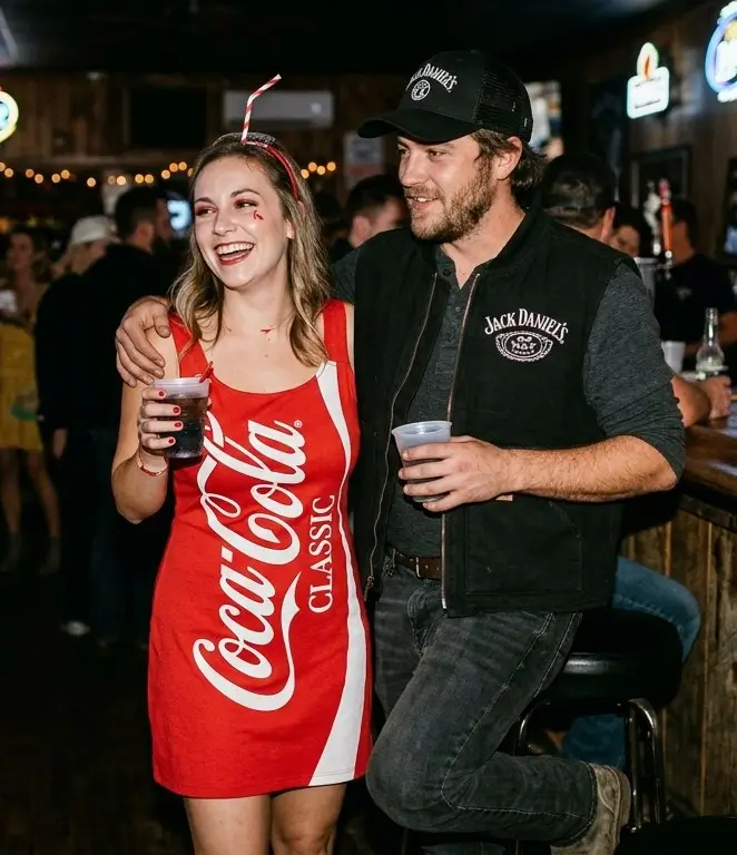 A smiling couple at a bar dressed in a Jack Daniel's and Coca-Cola themed costume, showing the easy DIY Jack and Coke halloween costume styled as a fun couple look