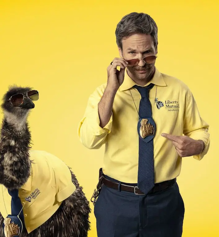 Limu Emu and Doug from the Liberty Mutual commercials standing together, Doug in his yellow shirt, tie, and aviator sunglasses with Limu Emu beside him