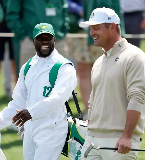 Kevin Hart wearing the official white Masters caddie jumpsuit and green cap while caddying for Bryson DeChambeau at the Augusta National Par 3 Contest