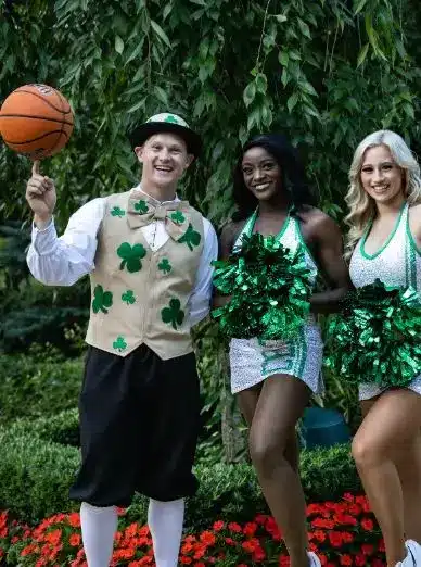 Lucky the Leprechaun mascot with Boston Celtics dancers at a game, showing the full costume in a court-side setting