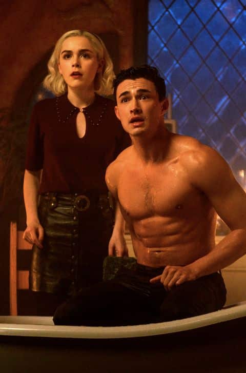 Nicholas Scratch and Sabrina Spellman from Chilling Adventures of Sabrina, showing the visual contrast between Nick's dark formal coat and Sabrina's red coat for a couples Halloween costume pairing