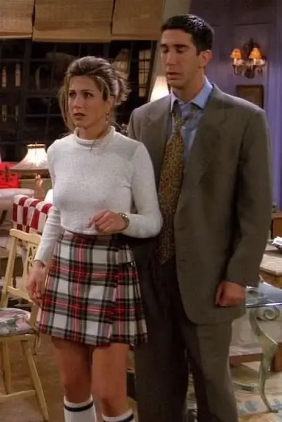 Rachel Green in a white top and Scottish plaid mini skirt with Ross Geller standing behind her in a grey suit, showing the Rachel and Ross couples Halloween costume pairing