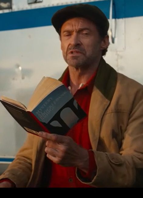 Hugh Jackman as George Hardy in The Sheep Detectives wearing a brown canvas jacket and newsboy cap while holding a shepherd's crook