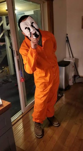 Fan cosplay of SCP-035 wearing an orange D-Class coverall with a white comedy and tragedy mask