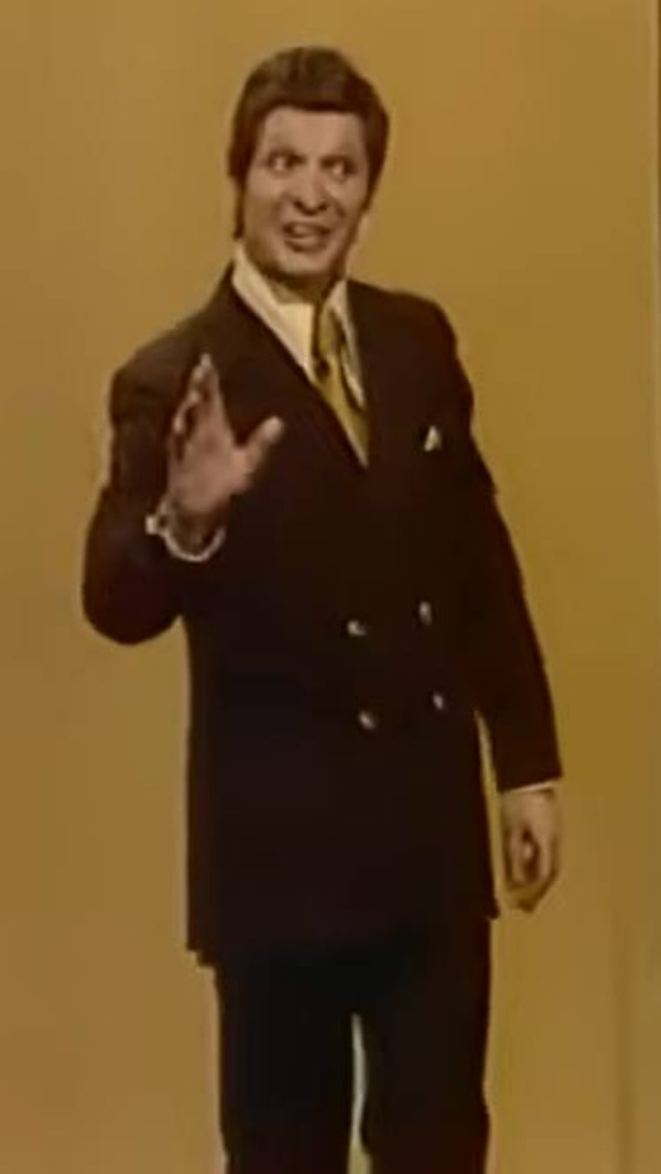Eduard Khil in the 1976 Trololo television performance wearing a dark double-breasted suit jacket with a gold tie and white pocket square