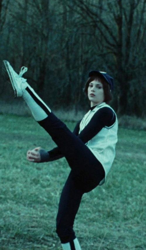 Alice Cullen in the Twilight baseball scene mid high-kick pitching wind-up, wearing the white and black jersey, stirrup socks, and navy cap