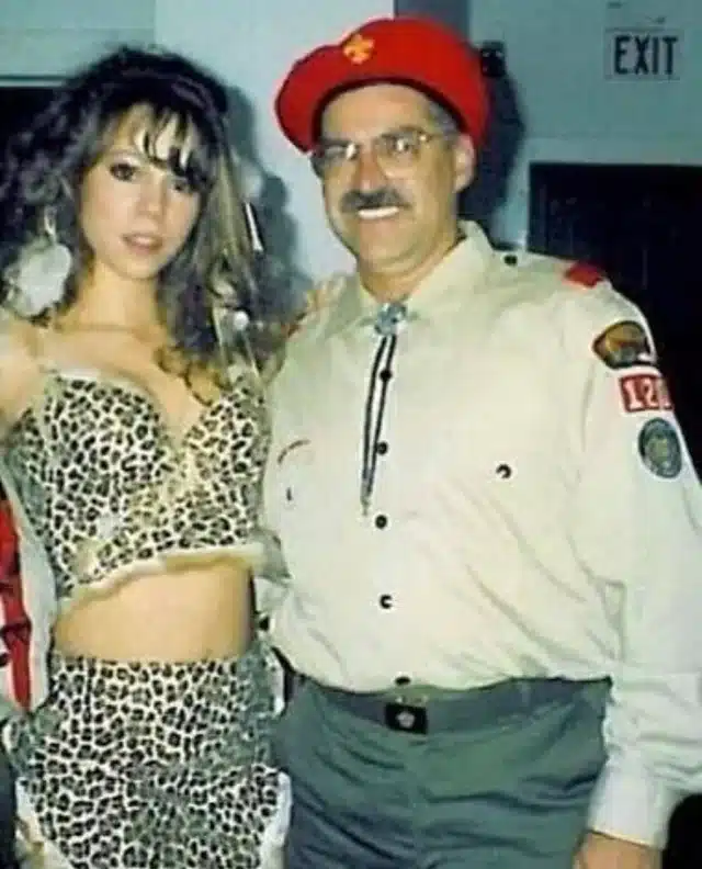 Mariah Carey in a cropped leopard print top and skirt posing with a costumed party guest for Halloween 1995
