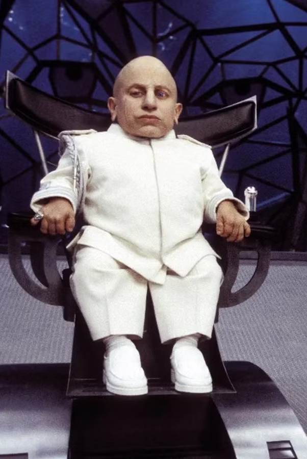 Mini Me sitting in a command chair, bald head and white Nehru-collar suit, reference image for the Halloween costume