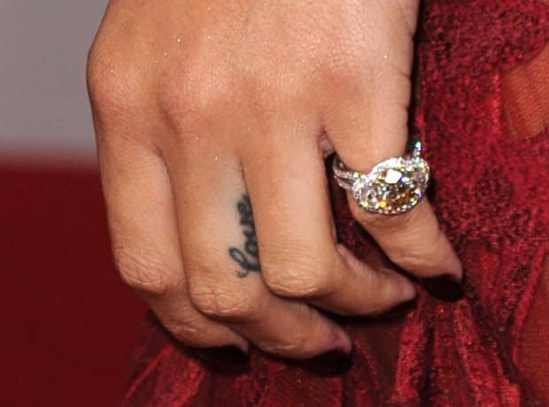 Small cursive Love tattoo on the side of Rihanna's middle finger