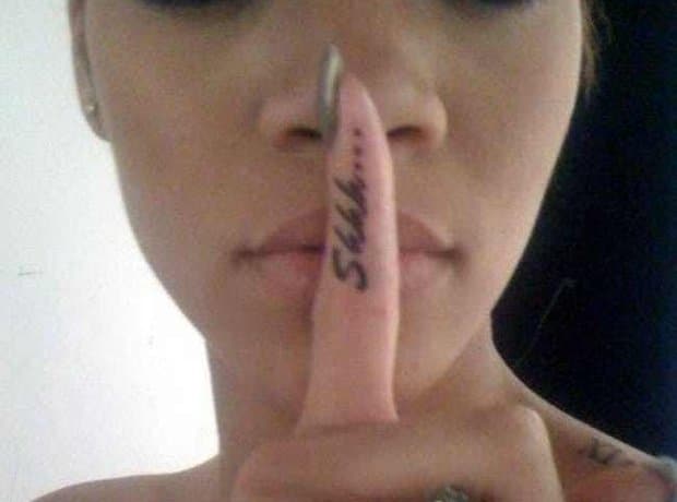 Rihanna holding her index finger to her lips to show the word Shhh tattooed along the side of the finger